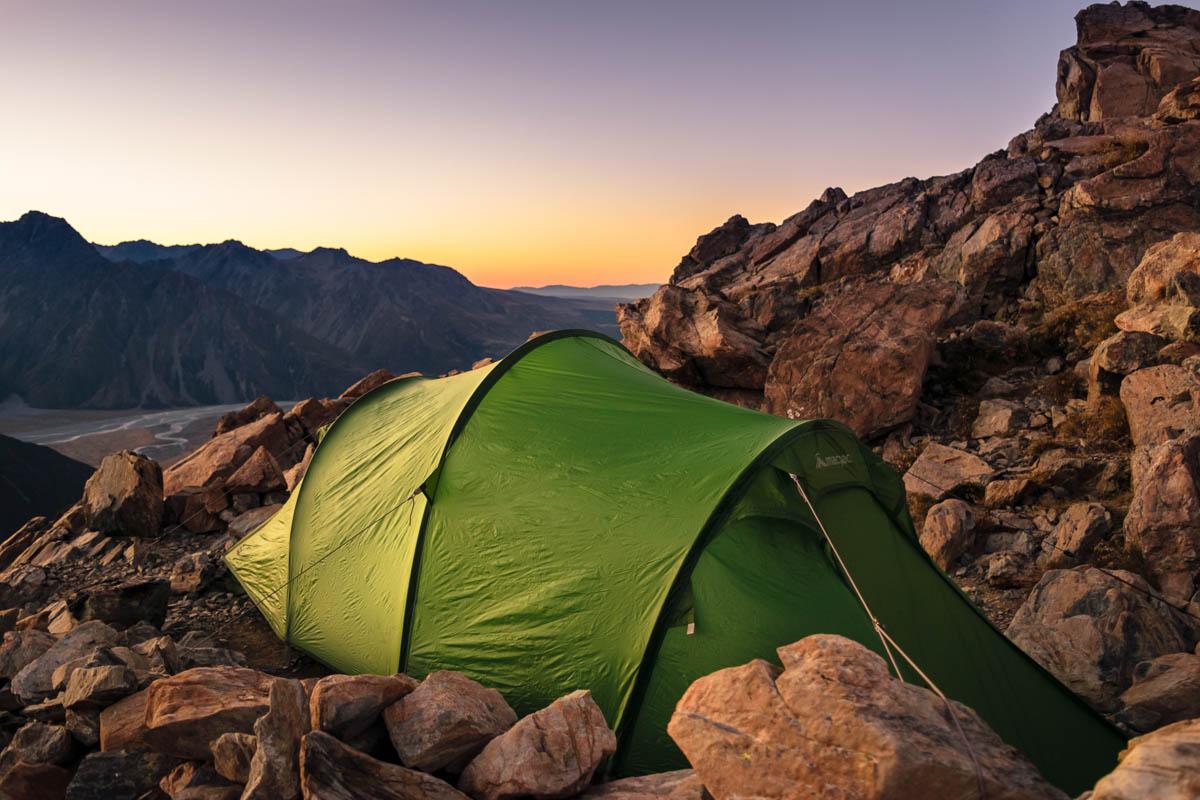 green eight person tent in the middle of rocks