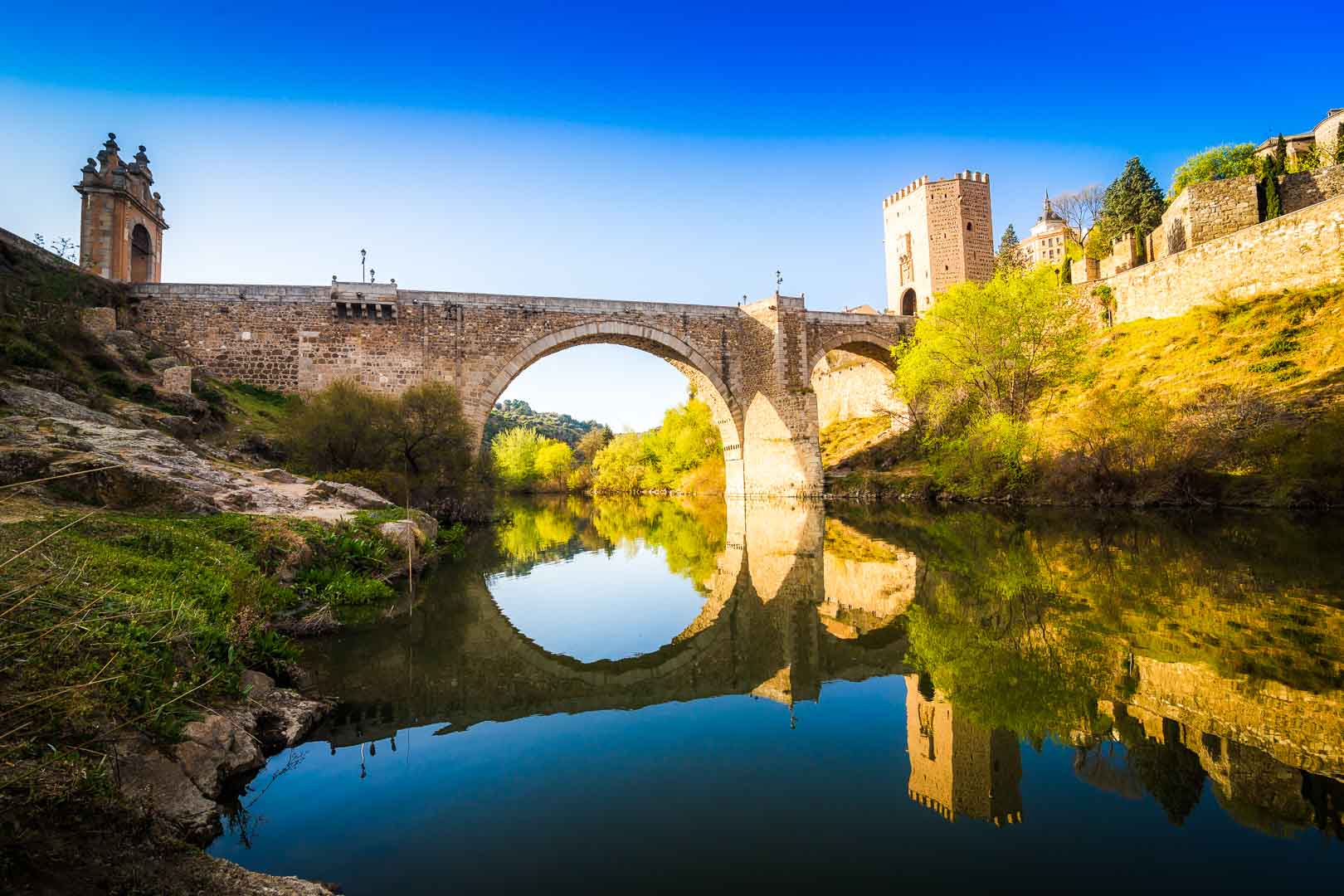 the puente de alcantara as seen from the river bank below